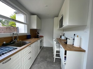 A compact kitchen with white cabinets, a wooden countertop, a built-in oven, and a window providing natural light.