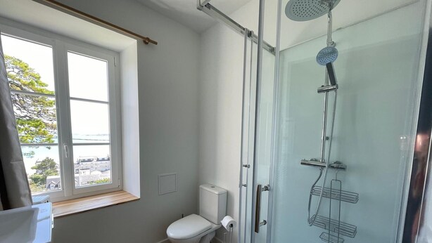Ein modernes Badezimmer mit Duschkabine aus Glas, Toilette und Fenster mit Blick auf Gebäude.