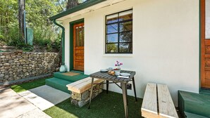 Une petite maison avec un mur en pierre, une porte en bois, une fenêtre et une table avec des sièges pour l’extérieur.