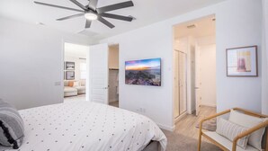 A bedroom with a bed, a ceiling fan, a TV, and a chair.