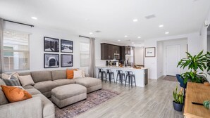 A modern living room with a sectional sofa, a small kitchen area, and a dining table with chairs.