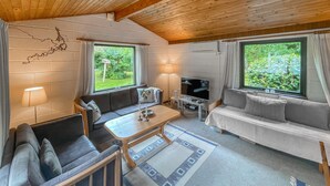 Een gezellige woonkamer met een bank, een salontafel, een televisie en grote ramen met uitzicht op groen.