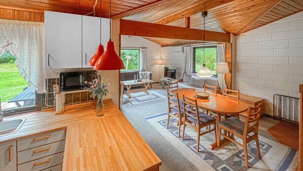 Een moderne keuken met houten kastjes, een eethoek met een houten tafel en stoelen, en een gezellige zithoek met een bank en televisie.