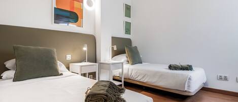 A hotel room with two beds, each with a pillow and a lamp. There are wall art pieces above the beds and a light fixture on the wall.