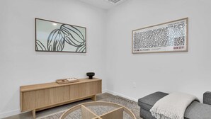 Een minimalistische woonkamer met een houten console, een grijze bank, een ronde salontafel en twee ingelijste kunstwerken aan de muur.