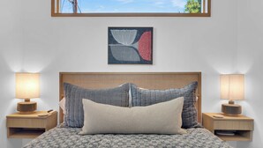 Een opgemaakt bed met een geborduurde spreidek, twee nachtlampjes en een lijst met abstracte kunst aan de muur.