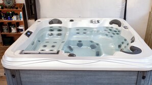 A hot tub with multiple jets, a control panel, and a wooden deck surrounding it. - 2 bedroom/2 bath w/hot tub & fire pit & outdoor living room (Candler)