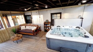 A wooden deck with a hot tub, a bed with pillows, a small table with a plant, and a shelf with various items. - 2 bedroom/2 bath w/hot tub & fire pit & outdoor living room (Candler)