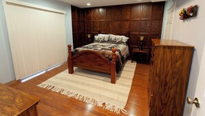 A bedroom with a wooden bed, a nightstand, a dresser, and a window with blinds. - 2 bedroom/2 bath w/hot tub & fire pit & outdoor living room (Candler)