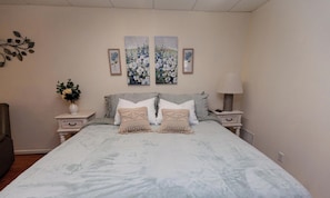 Ein Schlafzimmer mit einem Bett, zwei Nachttischen, einer Lampe und drei floralen Bildern an der Wand.