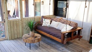 A wooden deck with a wooden swing bed, a round wooden table with a plant, and a window with a view of the outdoors. - 2 bedroom/2 bath w/hot tub & fire pit & outdoor living room (Candler)