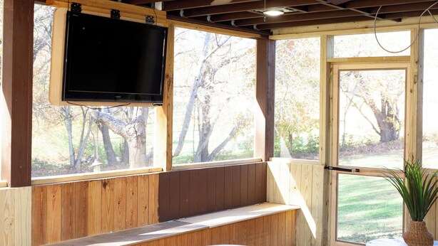 A wooden room with a TV mounted on the wall, a bench, and a window with a view of trees. - 2 bedroom/2 bath w/hot tub & fire pit & outdoor living room (Candler)