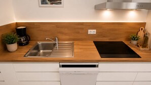 A modern kitchen with a stainless steel sink, a Bosch dishwasher, a black induction cooktop, and wooden countertops.