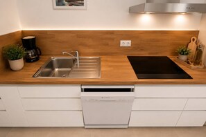 A modern kitchen with a stainless steel sink, a Bosch dishwasher, a black induction cooktop, and wooden countertops.