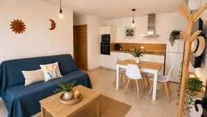 A modern kitchen with white cabinets, a wooden dining table, and a blue sofa with a 'LOVE' pillow.