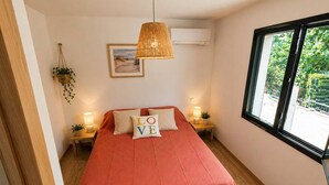 A bedroom with a bed, a hanging lamp, a window, and a wall-mounted air conditioner.