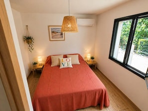 A bedroom with a bed, a hanging lamp, a window, and a wall-mounted air conditioner.