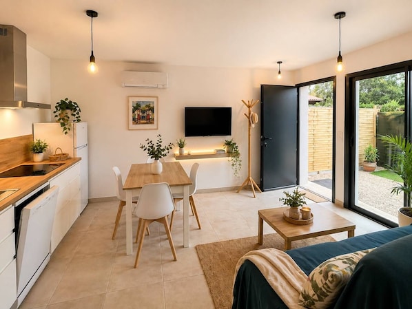 A compact kitchen with a dining area, a flat-screen TV, and a sliding glass door leading to a garden.