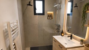 A modern bathroom with a shower, a sink, a mirror, a radiator, and a washing machine.