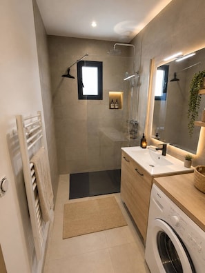 A modern bathroom with a shower, a sink, a mirror, a radiator, and a washing machine.