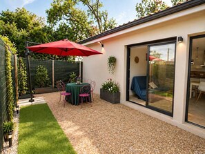 A patio with a table and chairs, a red umbrella, and a glass door leading to an interior space.