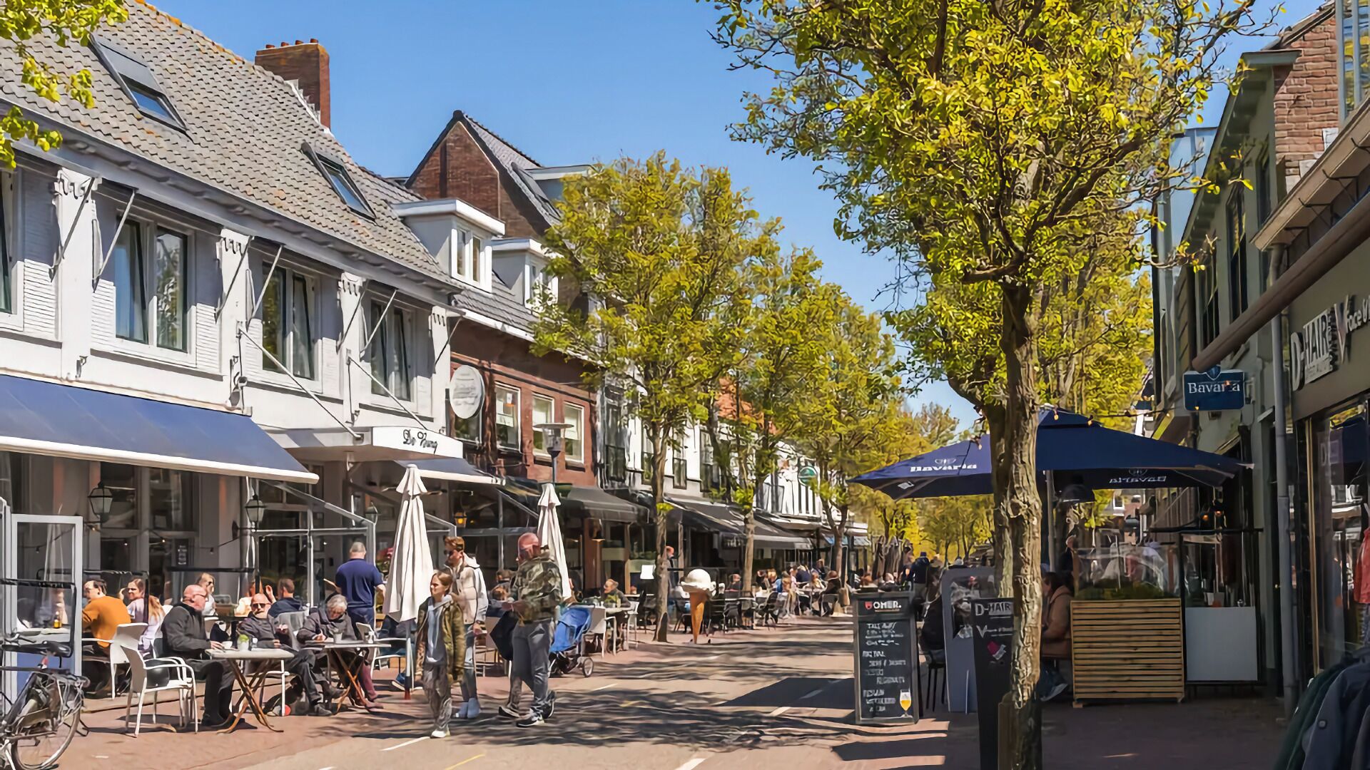 Une rue bordée de cafés et de boutiques, avec des terrasses et des parasols.
