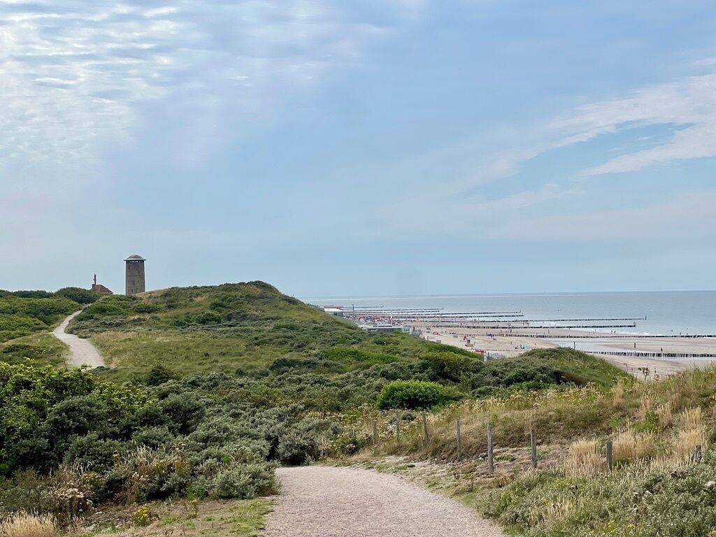 A coastal path leading to a beach with a lighthouse and a pier.