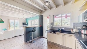 A modern kitchen with a built-in dishwasher, a bar area with a stool, and a window with a view of greenery. - Belle Maison vue montagnes (Bidarray)