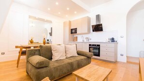 Een moderne woonkamer met een bank, een houten tafel en een keuken met kastjes en apparatuur.