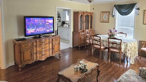 A living room with a television, wooden furniture, a ceiling fan, and a dining area with a table and chairs. - Magnolia Vacation Rental  w/ Porch & Pond (Senatobia)