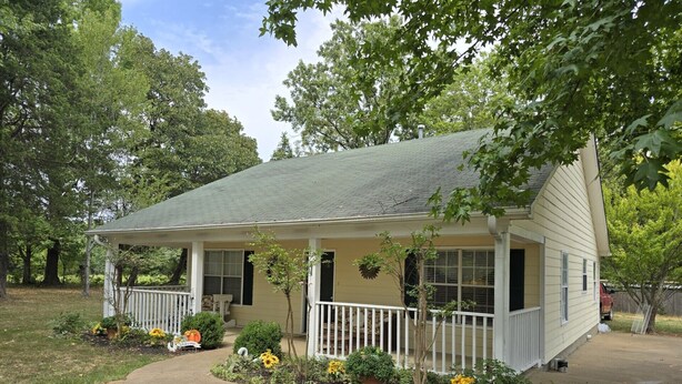 A single-story house with a porch, a small garden with sunflowers, and a clear sky. - Magnolia Vacation Rental  w/ Porch & Pond (Senatobia)