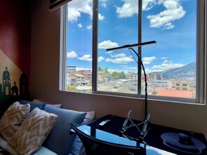 A room with a bed, a window with a view of buildings, and a table with a device. - Apartment with a Movie Theater, Ecuadorian Style, and Self-Check-In (Quito)