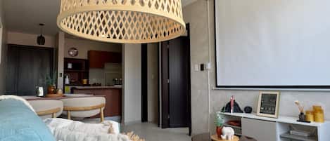 A modern living room with a large screen, a dining table, and a kitchen in the background.