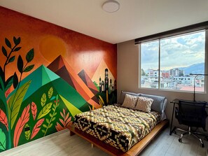 A bedroom with a bed, a window with a city view, and a colorful wall mural. - Apartment with a movie theater, Ecuadorian-style decor, and self-check-in (Quito)