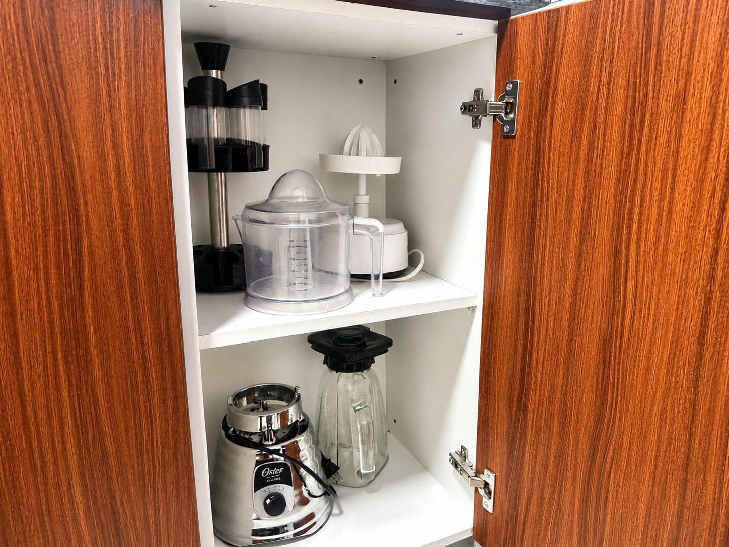 Un meuble de cuisine contenant une machine à café, un extracteur de jus et un mixeur, le tout placé sur les étagères.