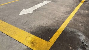 Une zone de stationnement avec des flèches indiquant le sens de circulation, une entrée fermée par une barrière et un panneau indiquant la sortie des véhicules.