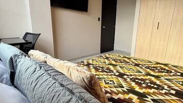 Een slaapkamer met een bed, een bureau, een stoel, een aan de muur bevestigde televisie en een kledingkast.