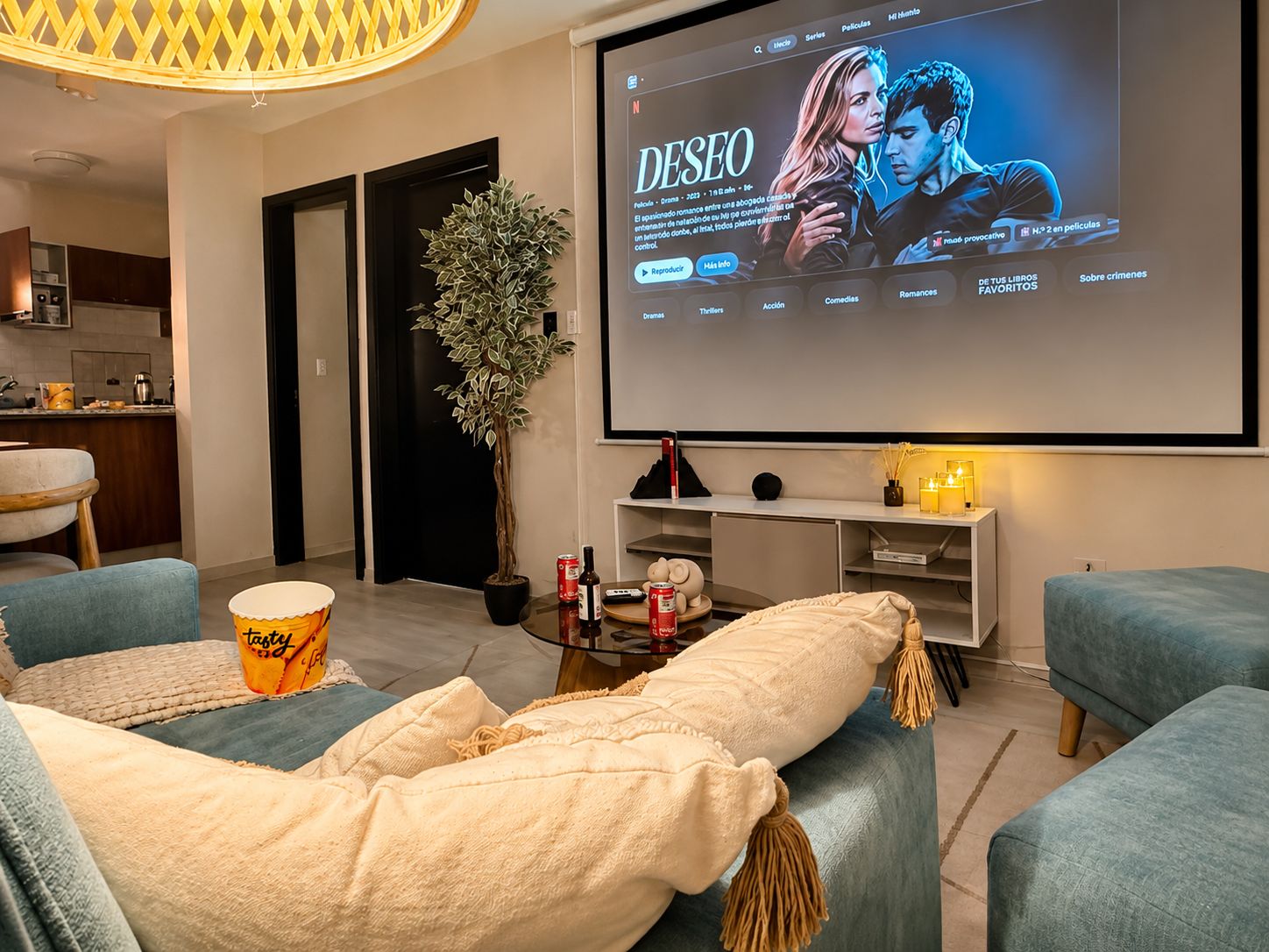 A living room with a large screen displaying a movie, comfortable seating, a small table with snacks, and a potted plant.