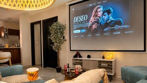 Un salon doté d’un grand écran diffusant un film, de sièges confortables, d’une petite table avec des collations et d’une plante en pot.