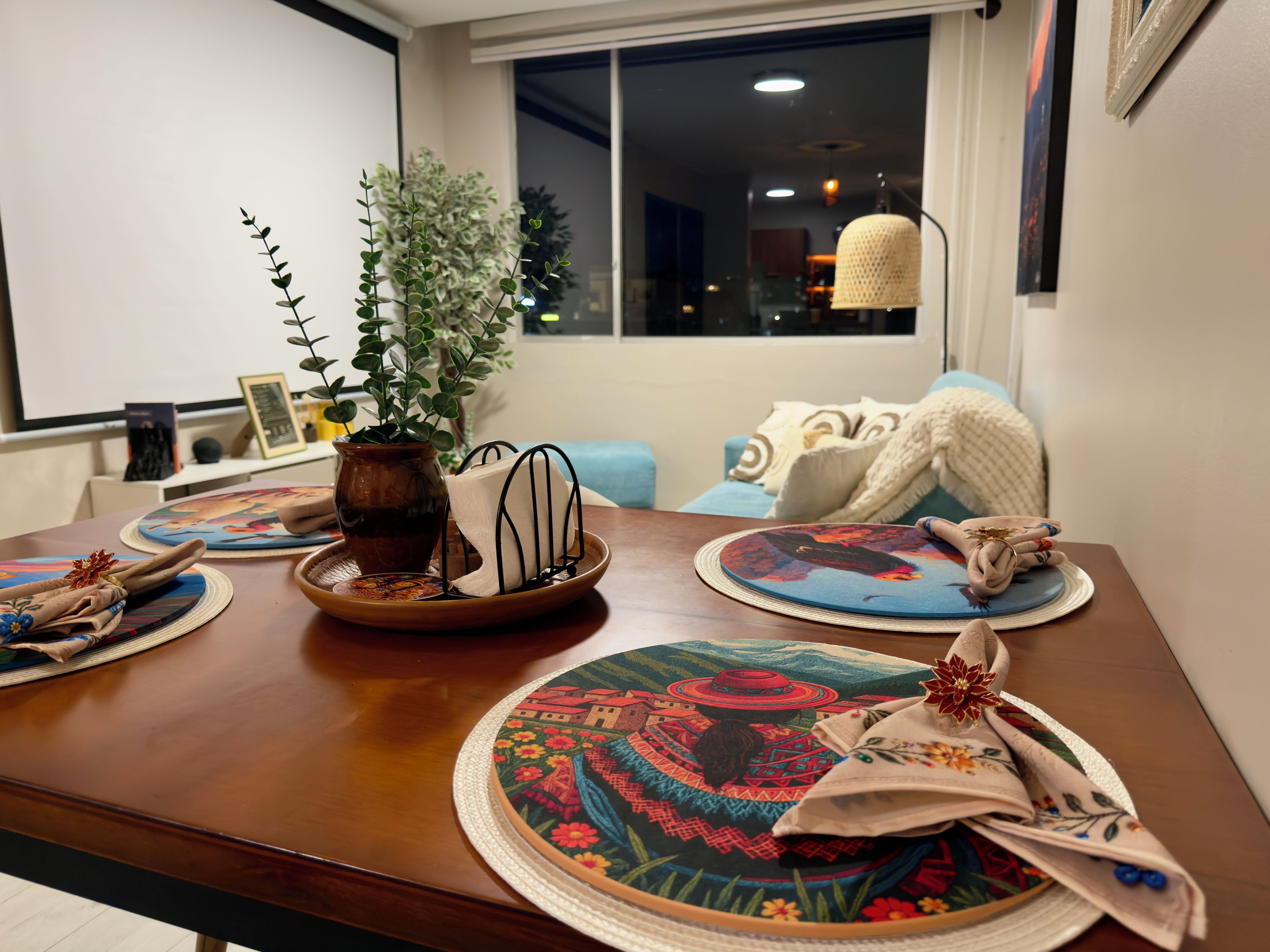 Una mesa de comedor con individuales, un jarrón con una planta y una ventana con vista a la ciudad de noche.