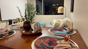 Una mesa de comedor con individuales, un jarrón con una planta y una ventana con vista a la ciudad de noche.