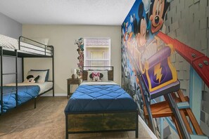 A room with bunk beds, a bed with a blue quilt, a window with blinds, and a wall mural.