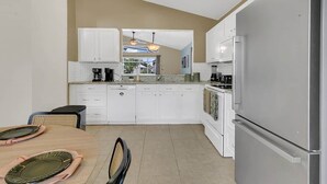 Una cocina moderna con armarios blancos, un refrigerador de acero inoxidable y un comedor con mesa y sillas.