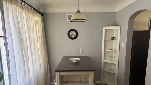 Una habitación con piso de madera, una mesa blanca con un tazón, un reloj, una estantería blanca y una puerta.