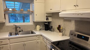 Una cocina moderna con armarios blancos, un lavamanos de acero inoxidable, horno empotrado y ventana con vista al jardín.