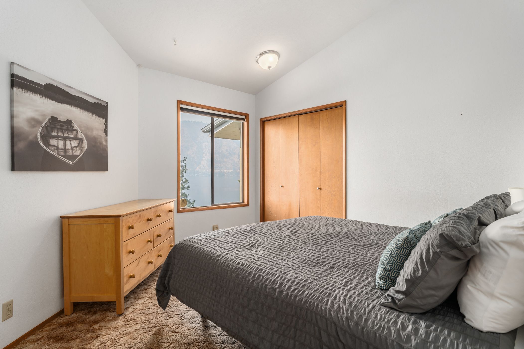 A bedroom with a bed, a wooden dresser, a window with a view, and a door.