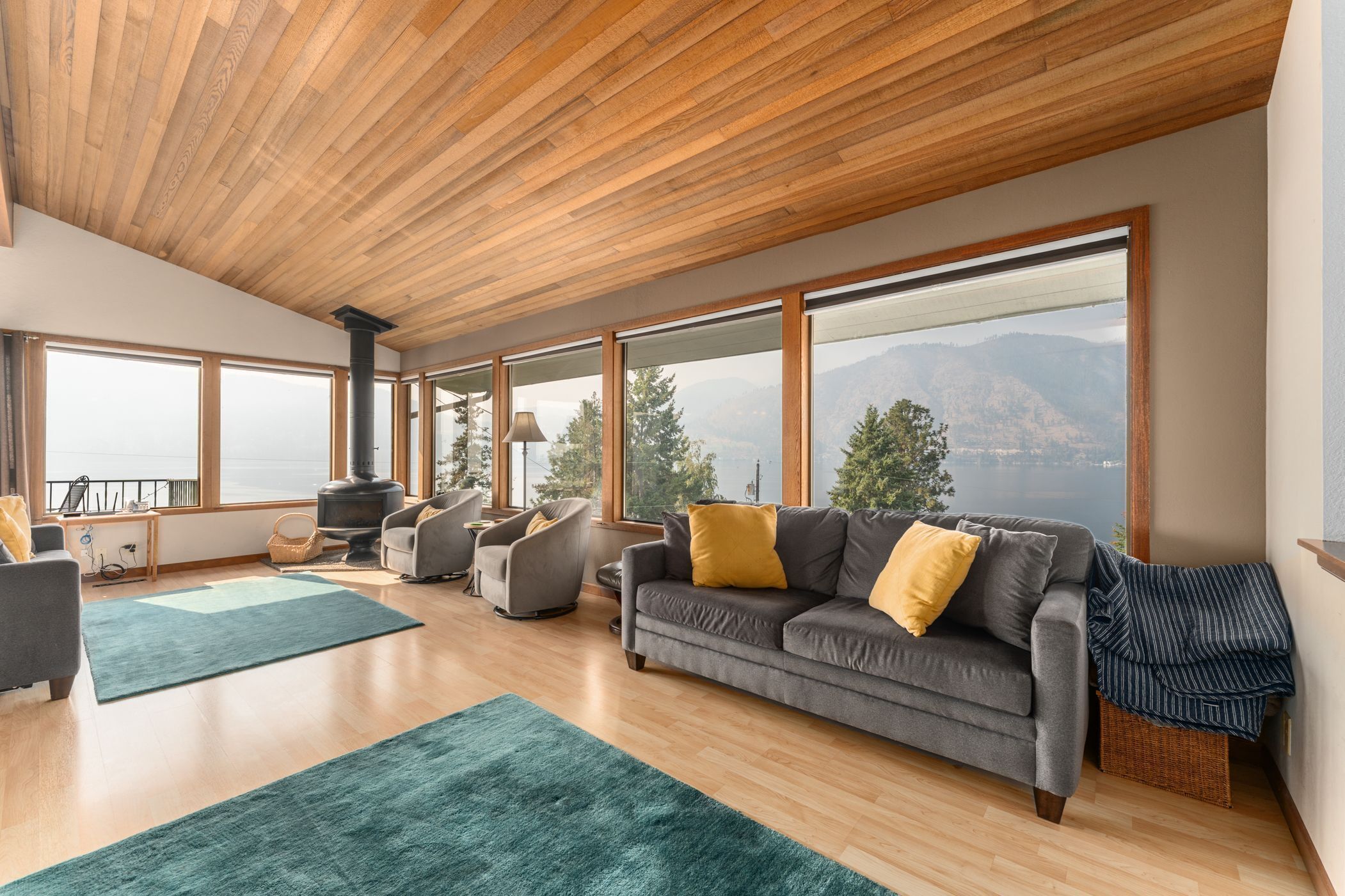 A spacious living room with a large gray sofa, a wooden ceiling, and large windows offering a mountain view.