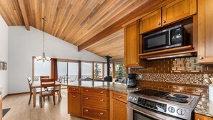 Une cuisine moderne avec des meubles en bois, une cuisinière en acier inoxydable et une grande fenêtre donnant sur un balcon.
