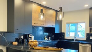 Une cuisine moderne avec des meubles de couleur sombre, un îlot central doté de tabourets de bar, un éclairage suspendu et une vue sur l’extérieur.