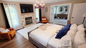 Un dormitorio amplio con una cama grande, chimenea, televisión y un baño visible a través de una puerta abierta.